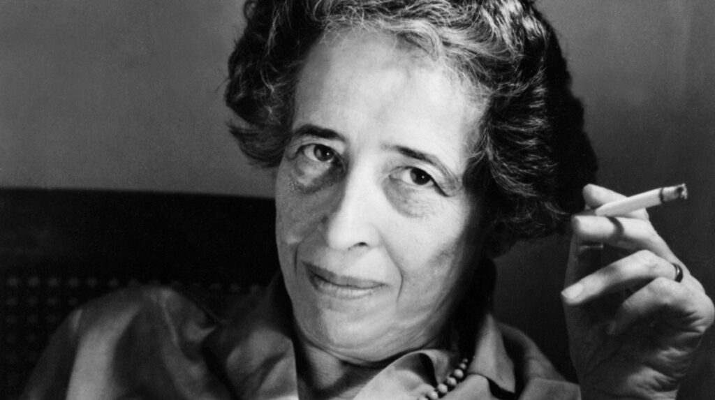 Hannah Arendt, eine bedeutende politische Theoretikerin, mit einer Zigarette in der Hand, in einem nachdenklichen Ausdruck.