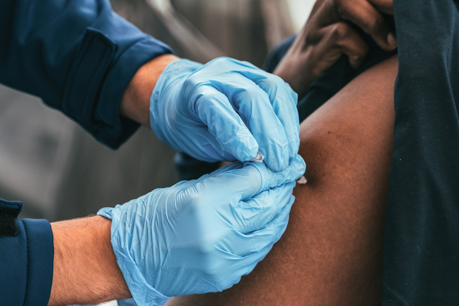 Arzt mit blauen Handschuhen verabreicht eine Impfung an den Oberarm eines Patienten.