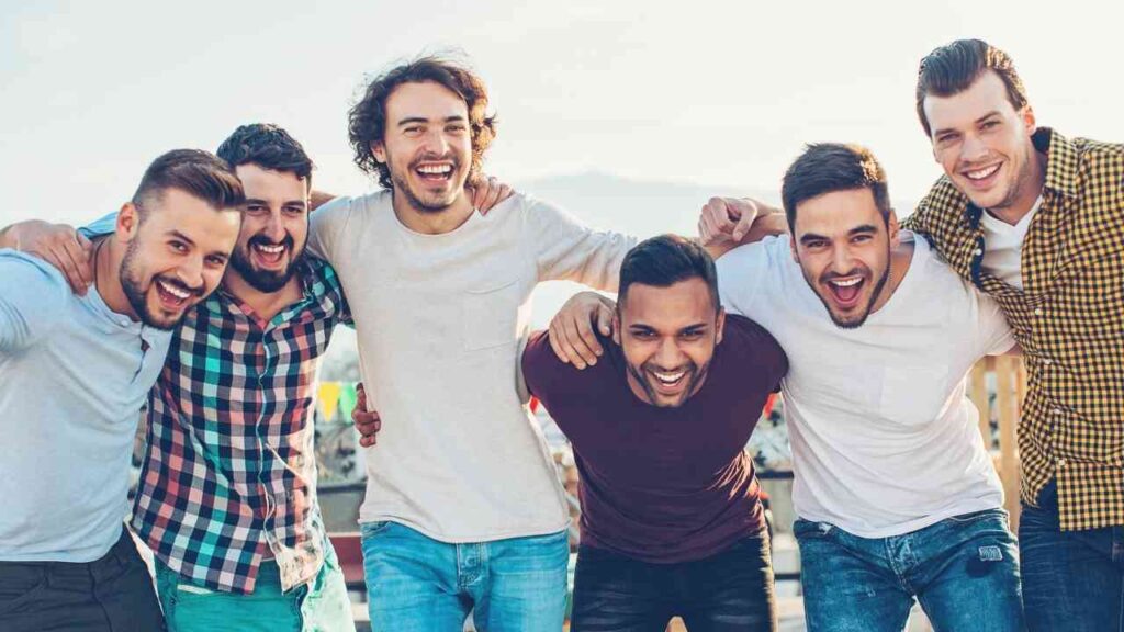 Sechs Männer stehen zusammen und lachen in einer fröhlichen Pose, während sie sich umarmen.
