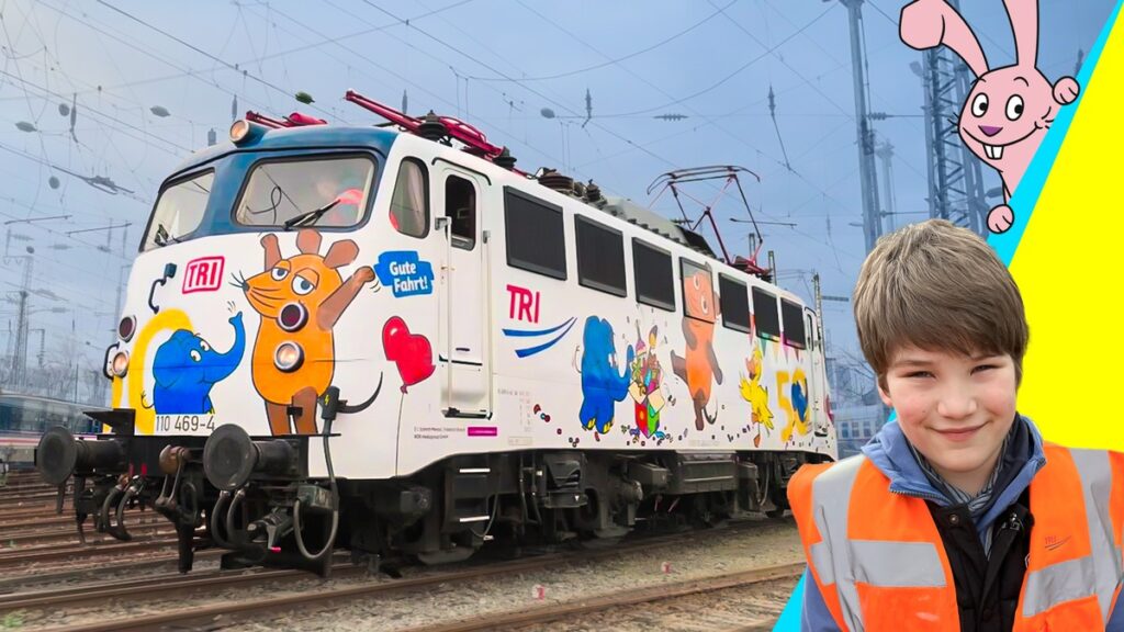Bunte Lokomotive mit Tiermotiven und einem Jungen in Warnweste, der lächelt.