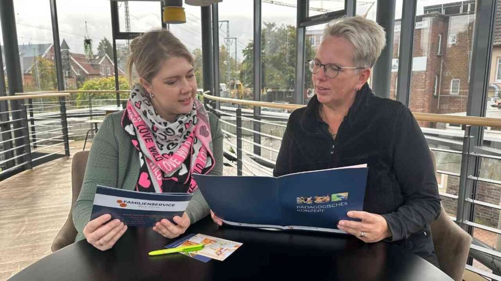 Zwei Frauen, die an einem Tisch sitzen und ein Informationsheft über pädagogische Konzepte betrachten.