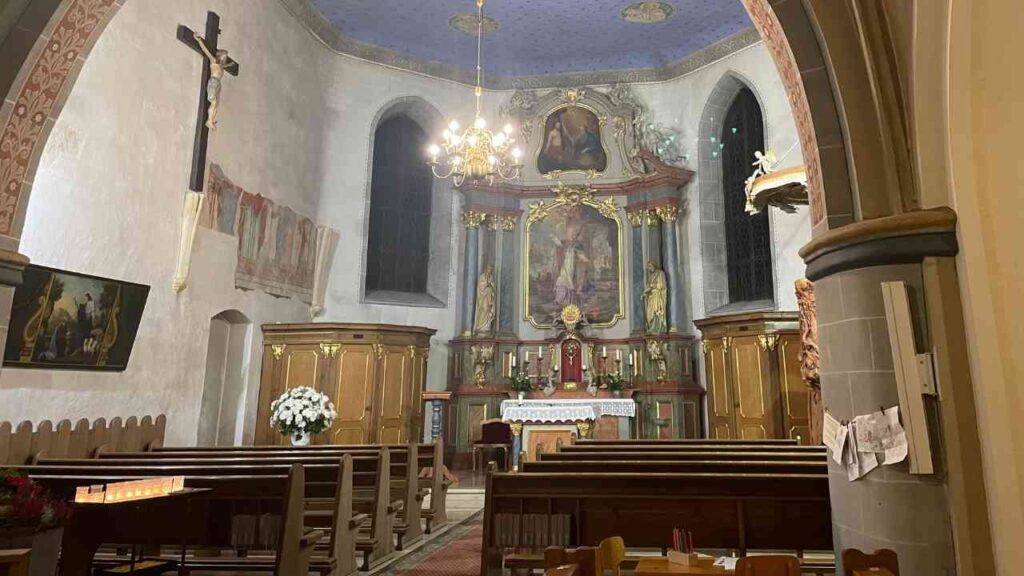Innenansicht einer Kirche mit Altar, Bänken und dekorativen Elementen.