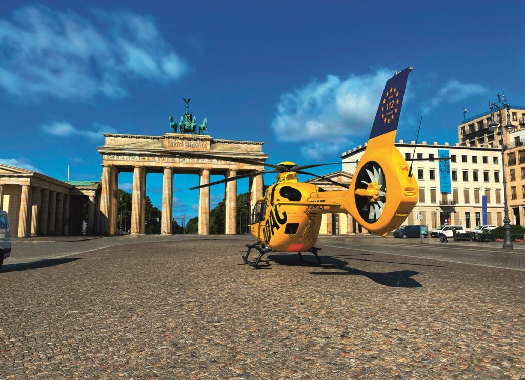 Gelber Hubschrauber vor dem Brandenburger Tor in Berlin, mit klarem Himmel und Wolken im Hintergrund.