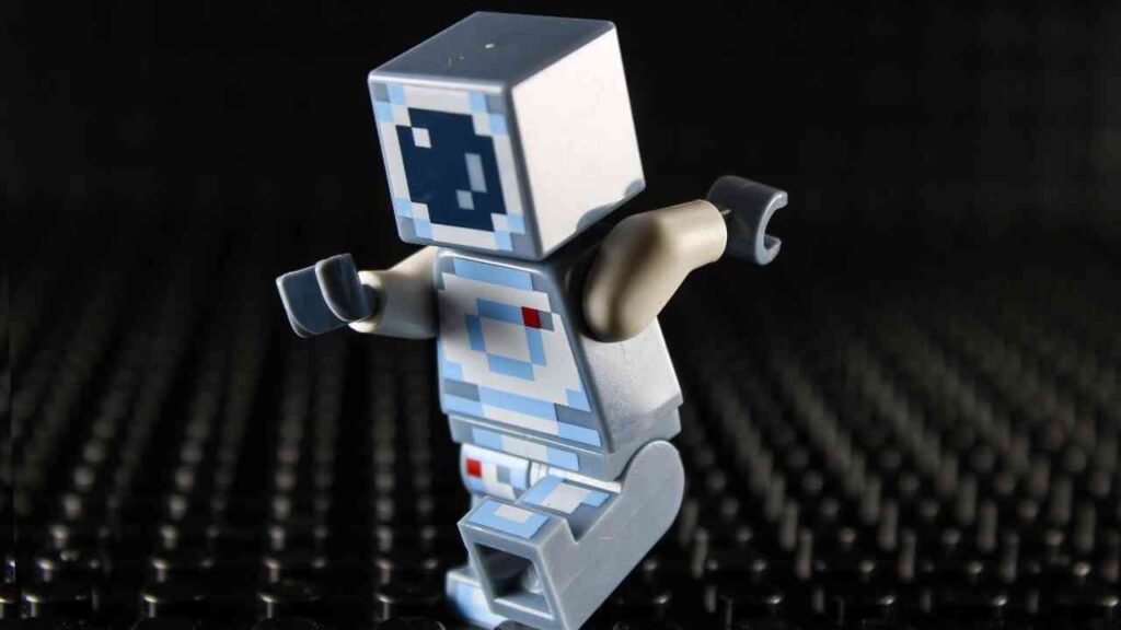 Mikro-Roboter mit einem quadratischen Kopf und einem blauen und grauen Design, auf einer schwarzen Oberfläche stehend.