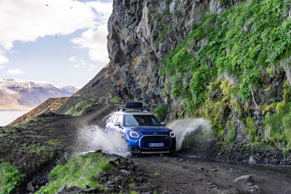Blauer Mini Countryman fährt auf einer unbefestigten Straße in Island und spritzt Wasser auf.