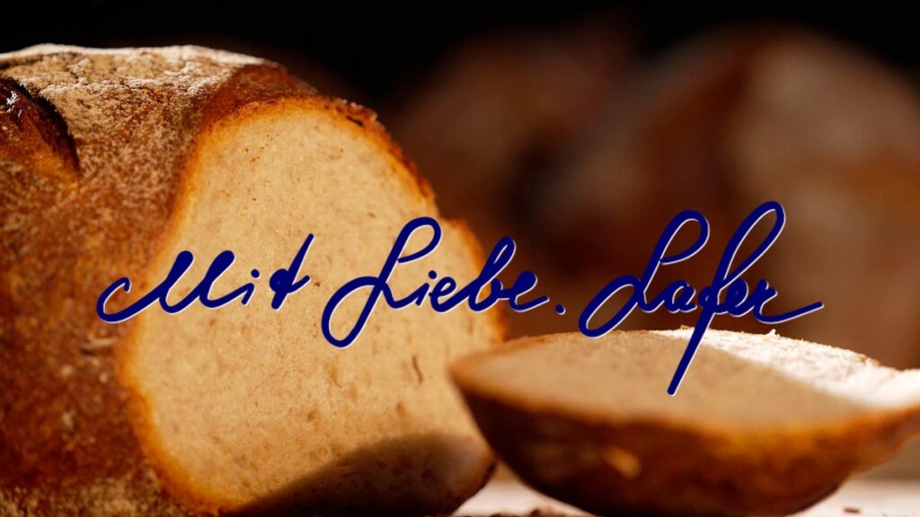 Ein Laib Brot mit einer aufgeschnittenen Scheibe und der Schriftzug 'Mit Liebe, Lafer' in blauer Schrift.