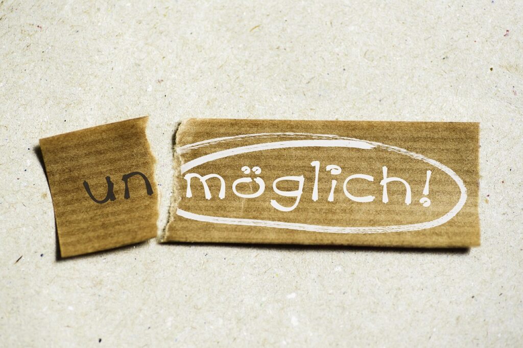 Ein Stück braunes Papier mit dem Wort 'un' und einem größeren Stück mit dem Wort 'möglich!' in einer kreativen Schriftart.