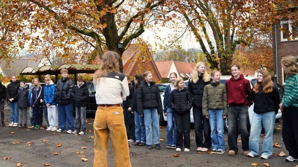 Gruppe von Jugendlichen in Winterjacken und Hosen, die in einer Reihe stehen und auf eine Person vor ihnen schauen.