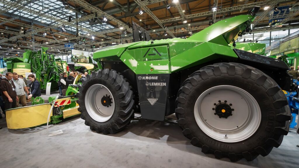 Großer grüner Traktor mit breiten Reifen auf einer landwirtschaftlichen Messe, umgeben von landwirtschaftlichen Maschinen.