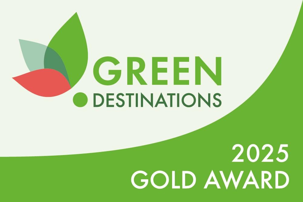 Logo der Green Destinations Gold Award 2025 mit grünen und roten Blättern auf hellem Hintergrund.