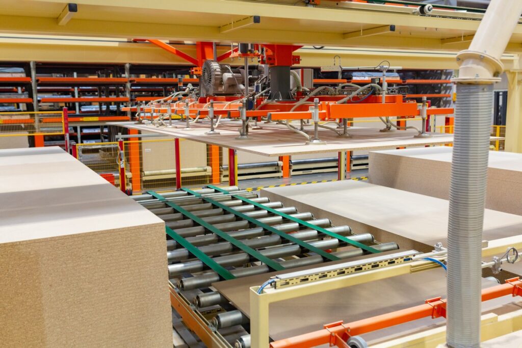 Automatisierte Maschinen in einer Produktionsanlage zur Verarbeitung von Holzplatten und Kartonagen.