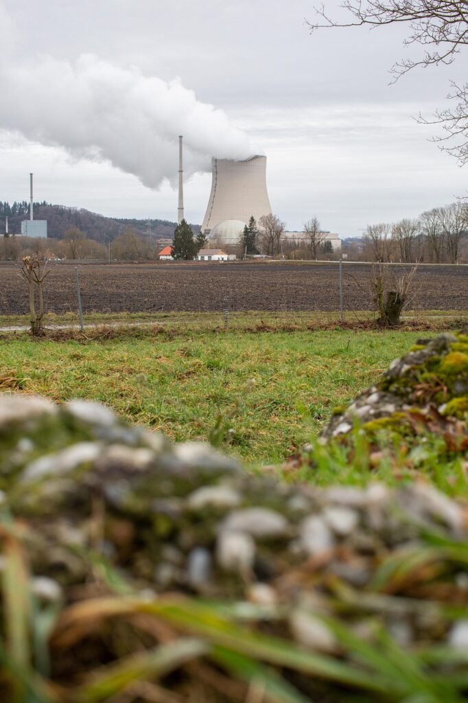 Kernkraftwerk mit Kühlturm und Rauchabzug, umgeben von landwirtschaftlicher Fläche.