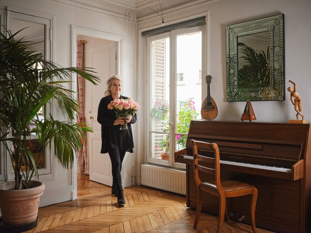 Frau mit einem Blumenstrauß in einem Raum mit Pflanzen und einem Klavier.