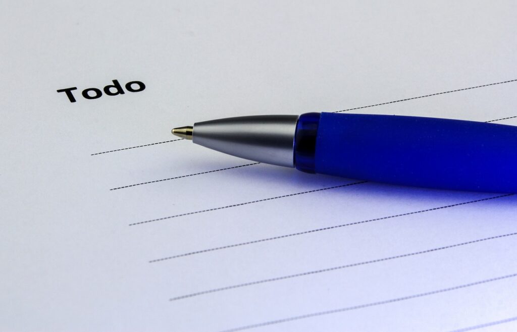 Blaue Kugelschreiber auf einem leeren Notizblatt mit der Aufschrift 'Todo'.