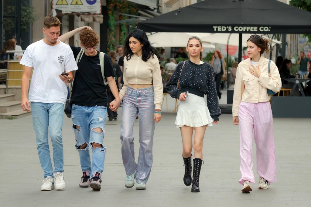 Fünf junge Menschen gehen entspannt auf einer Straße, während sie miteinander sprechen und ihre Smartphones benutzen.