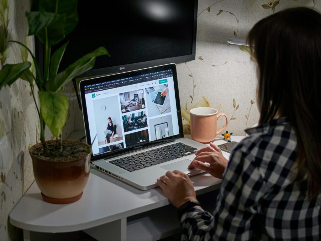Frau, die an einem Laptop mit Bildern arbeitet, während sie an einem Schreibtisch sitzt, umgeben von einer Pflanze und einer Tasse.