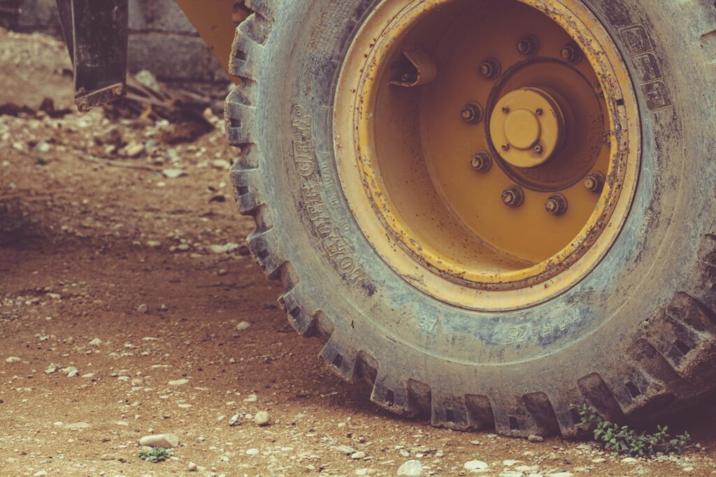 Reifen eines gelben Baumaschinenfahrzeugs mit grobem Profil auf unebenem Untergrund.