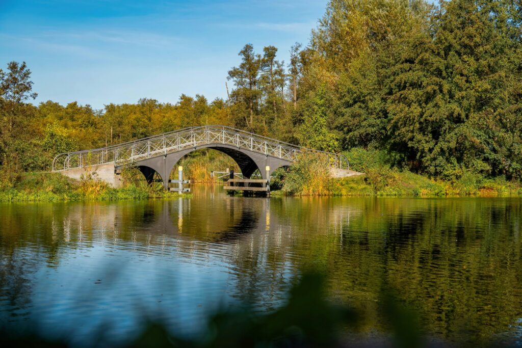 Brücke über einen ruhigen Wasserlauf mit reflektierenden Oberflächen und umgebender Vegetation.