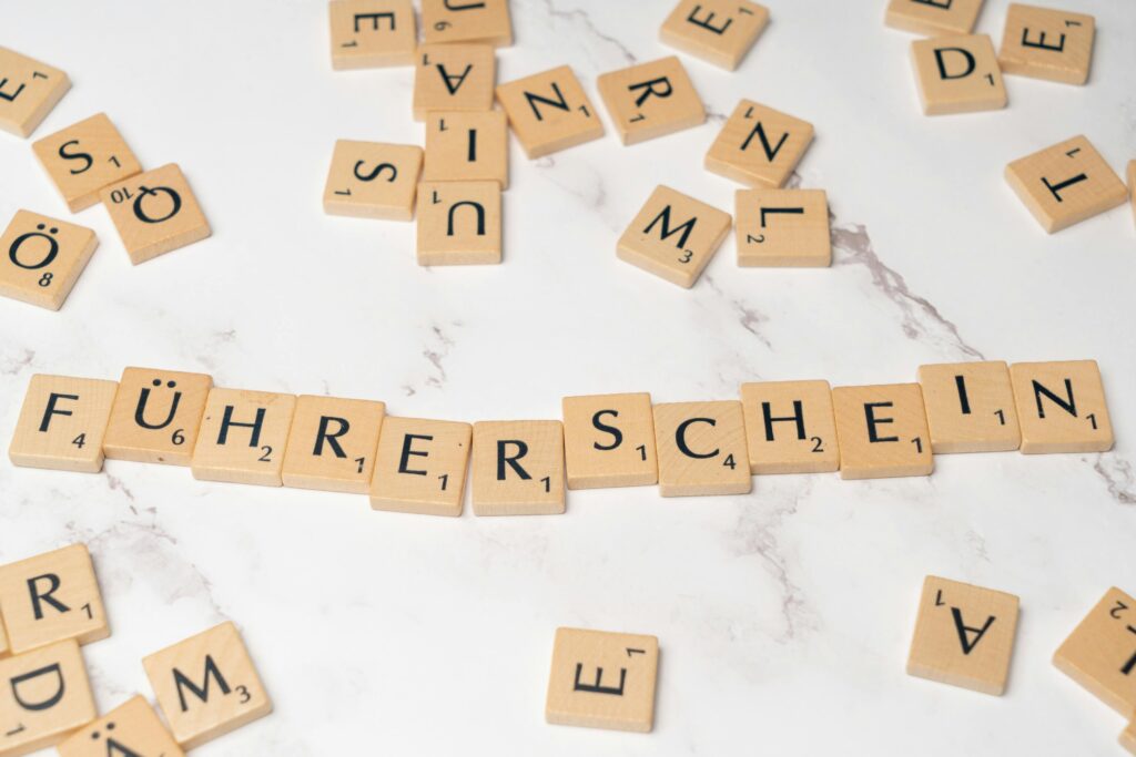 Holzbuchstaben auf einem Tisch, die das Wort 'Führerschein' bilden, umgeben von weiteren Buchstaben.
