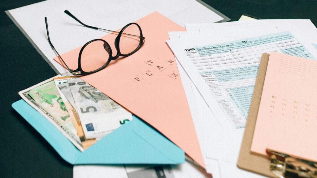 Brille auf einem Stapel von Dokumenten, darunter Geldscheine und Steuerformulare.