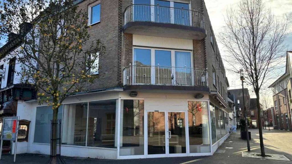 Eckgebäude mit großen Fenstern und Balkon in einer städtischen Umgebung.