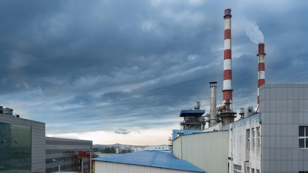 Industrieanlage mit zwei hohen Schornsteinen und grauem Himmel, der von Wolken bedeckt ist.