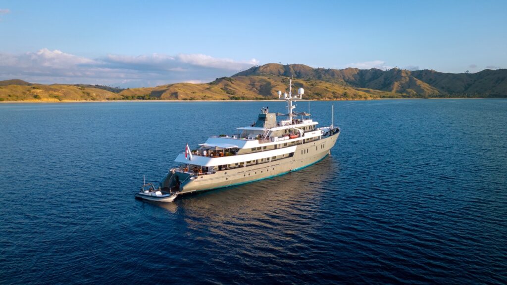Luxuriöses Kreuzfahrtschiff auf ruhigem Wasser mit grünen Hügeln im Hintergrund.