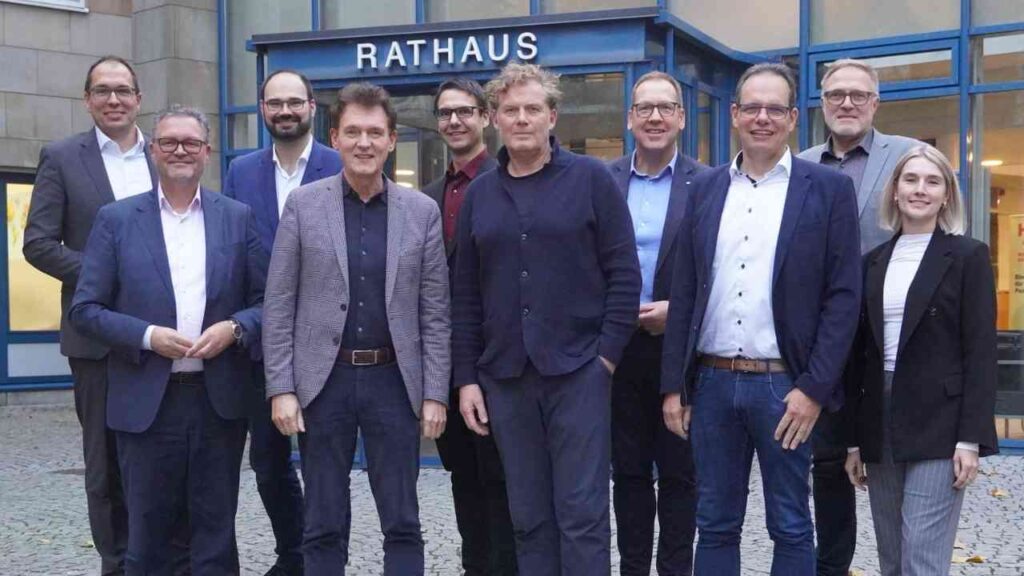 Gruppe von Personen vor dem Rathaus, die in formeller Kleidung stehen und in die Kamera schauen.