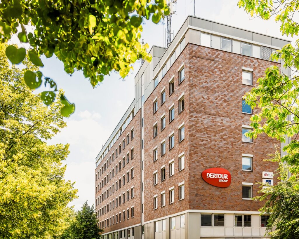 Gebäude der Dertour Group mit rotem Logo an der Fassade, umgeben von Bäumen und blauem Himmel.