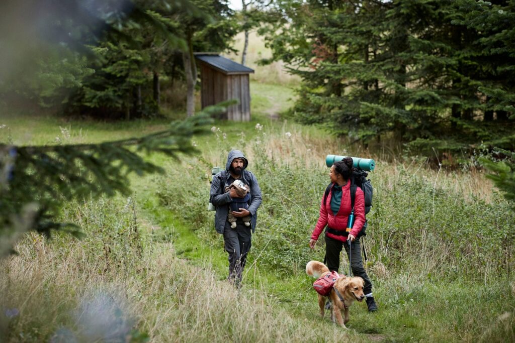 Zwei Wanderer mit Rucksack und Hund auf einem Waldweg in der Natur.