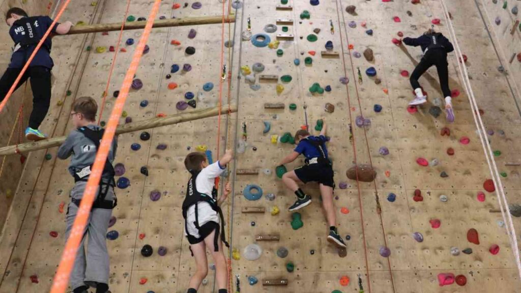 Kinder, die an einer Kletterwand mit bunten Griffen in einer Kletterhalle klettern.