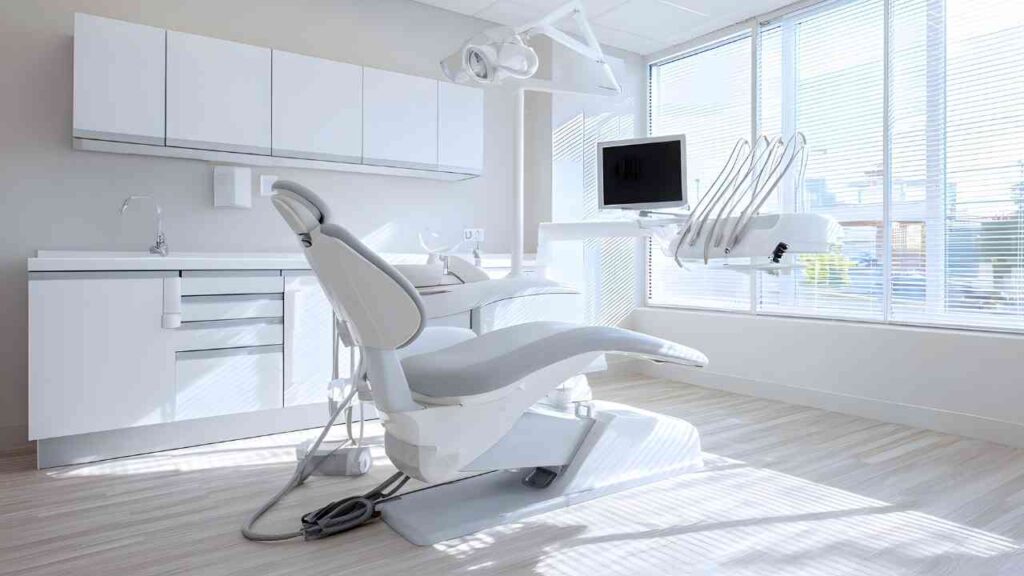 Moderne Zahnarztpraxis mit einem Behandlungsstuhl, einem Monitor und hellen Fenstern.