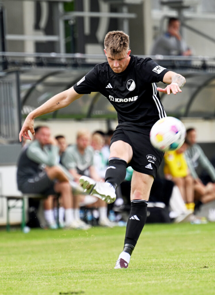 Fußballspieler in schwarzem Trikot, der einen Schuss auf das Tor abgibt während eines Trainings.
