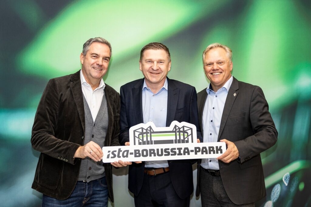 Drei Männer halten ein Schild mit der Aufschrift 'ista-Borussia-Park' und posieren für ein Foto.