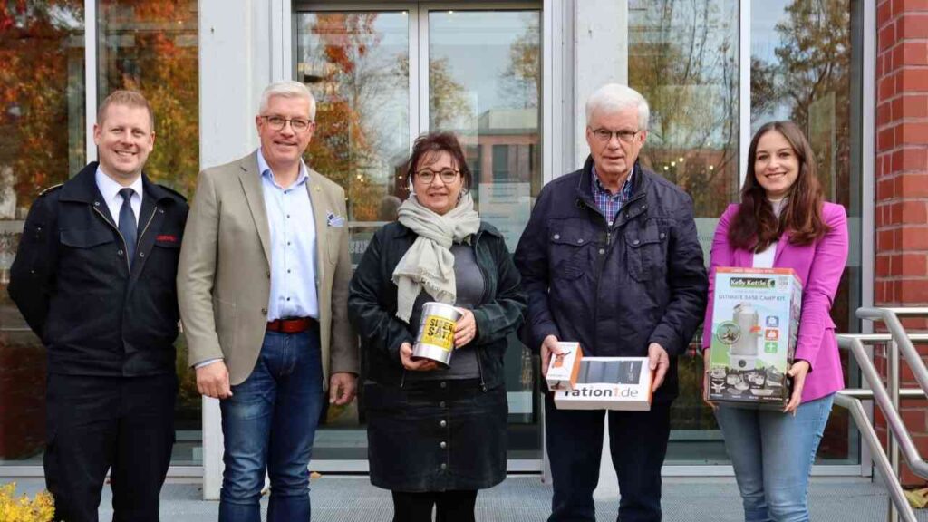 Fünf Personen stehen vor einem Gebäude, jede hält verschiedene Gegenstände in den Händen.