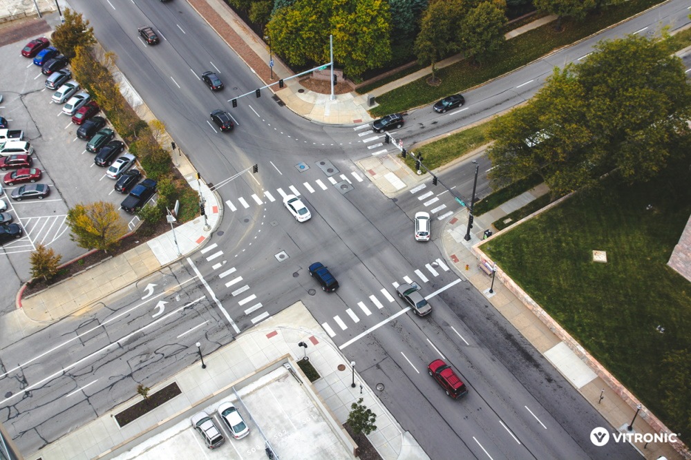 Luftaufnahme einer Straßenkreuzung mit Fahrzeugen und Fußgängerüberwegen in einer urbanen Umgebung.