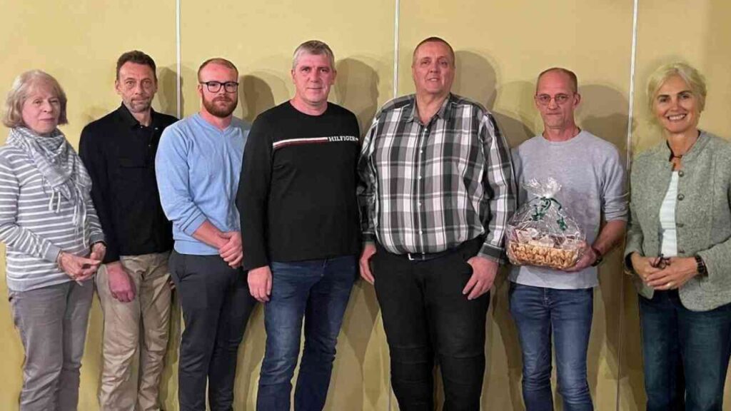 Gruppe von sieben Personen, die in einem Innenraum stehen, einige halten eine Geschenkbox.