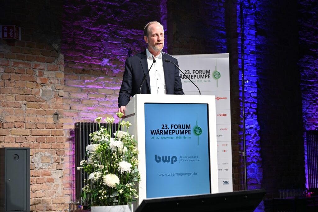 Mann steht am Rednerpult beim 23. Forum Wärmepumpe in Berlin, umgeben von Pflanzen und einer Präsentation.