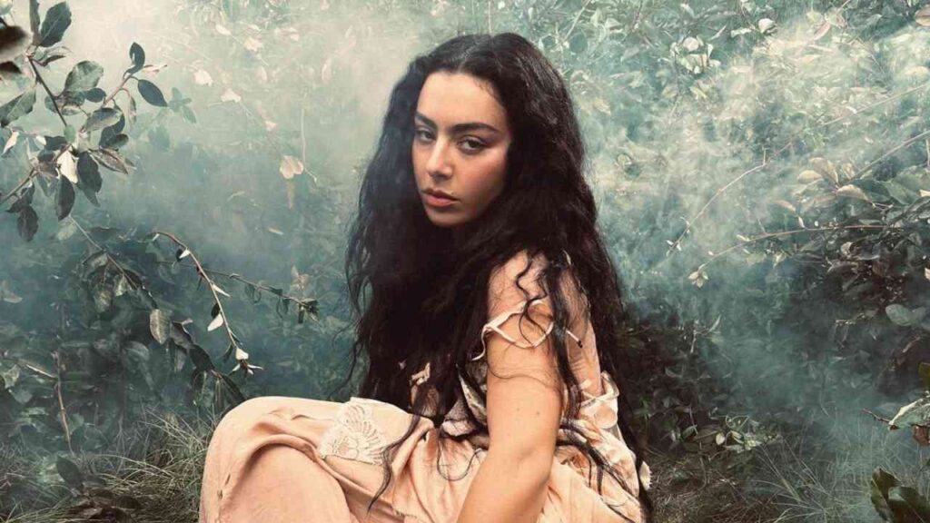 Frau mit langen, dunklen Haaren in einem fließenden Kleid, umgeben von Pflanzen und Nebel.