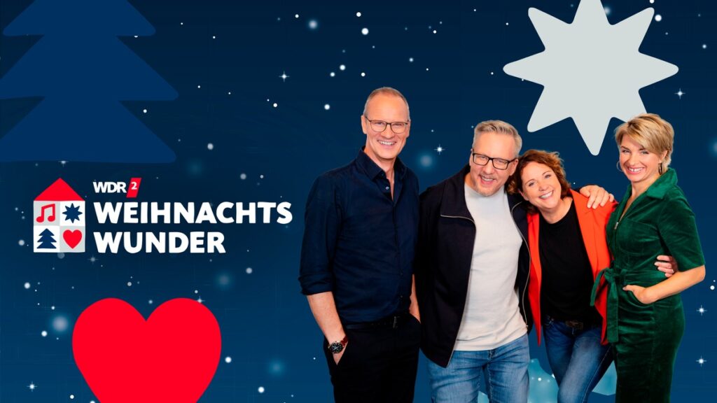 Vier Personen posieren zusammen vor einem blauen Hintergrund mit Weihnachtsmotiven und dem Text 'WDR 2 Weihnachtswunder'.