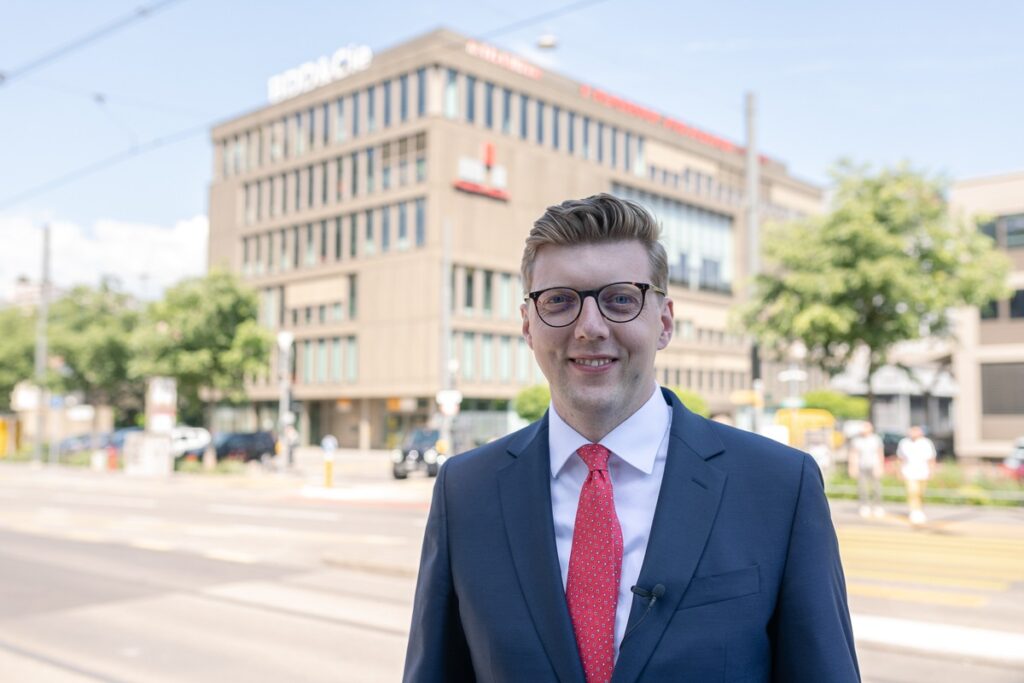 Mann in Anzug mit roter Krawatte steht vor einem modernen Gebäude in Köln.