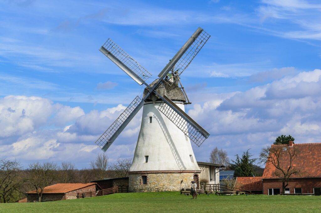 Windmühle mit weißen Flügeln und einem traditionellen Steingebäude im Hintergrund unter einem blauen Himmel.