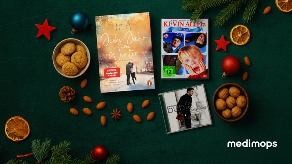 Buchcover von 'Ein Jahr im Winter' von Emily Stone, DVD von 'Kevin allein zu Haus' und Weihnachts-CD auf einem Tisch mit Keksen und Nüssen.
