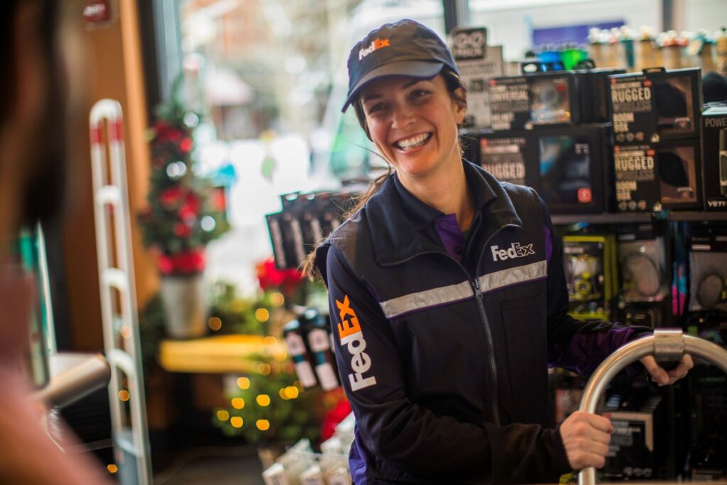 FedEx-Mitarbeiterin lächelt freundlich in einem Geschäft mit verschiedenen Produkten im Hintergrund.