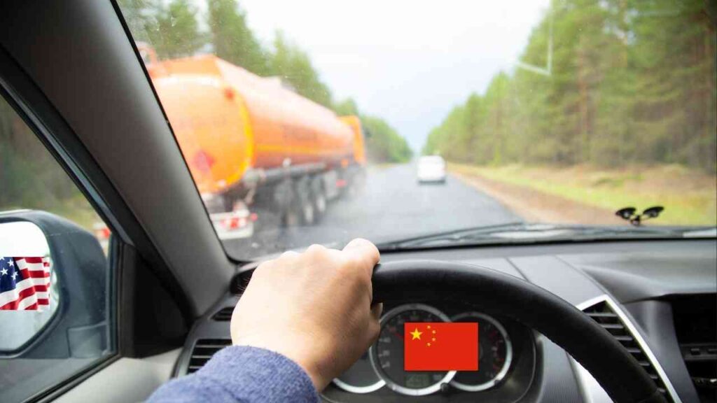 Fahrersicht aus einem Auto mit einer Hand am Lenkrad und einem Lkw im Hintergrund auf einer Straße.