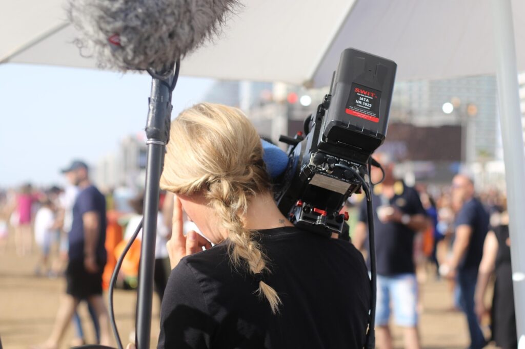 Frau mit Kamera und Mikrofon, die bei einer Veranstaltung im Freien filmt.