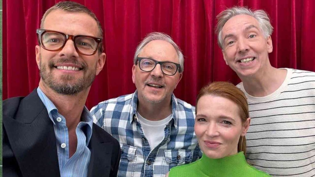 Vier Personen posieren lächelnd für ein Selfie vor einem roten Hintergrund.