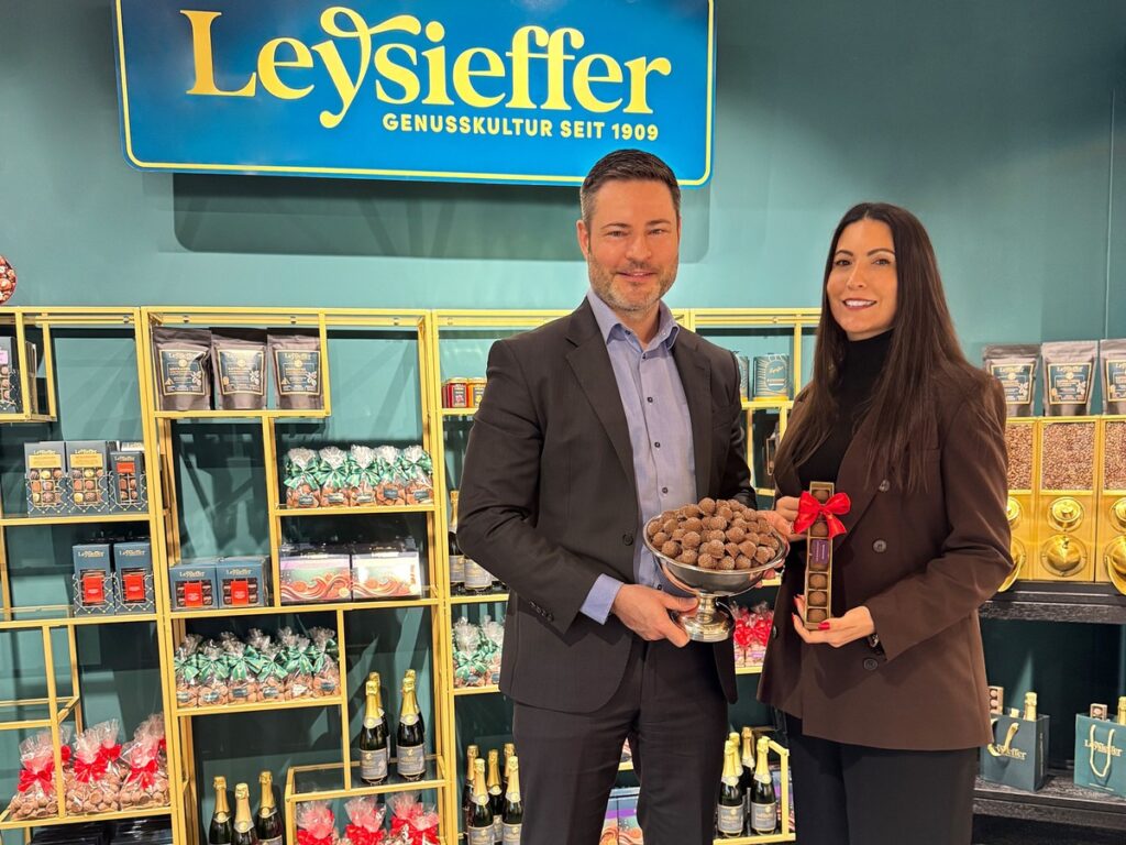 Zwei Personen halten eine Schüssel mit Pralinen und eine Auszeichnung in einem Geschäft von Leysieffer.