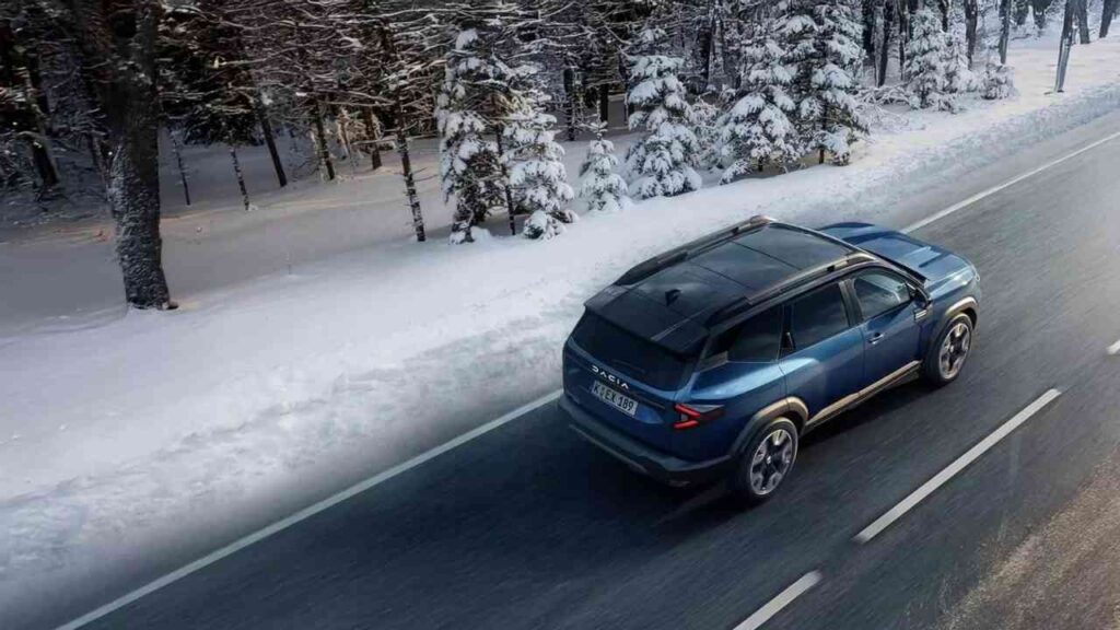 Blauer SUV fährt auf einer schneebedeckten Straße durch einen winterlichen Wald.