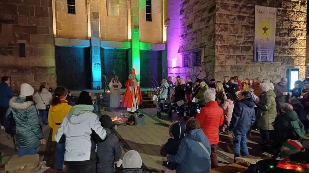 Eine Gruppe von Menschen versammelt sich um eine Darbietung im Freien, während ein Darsteller in festlicher Kleidung auftritt.